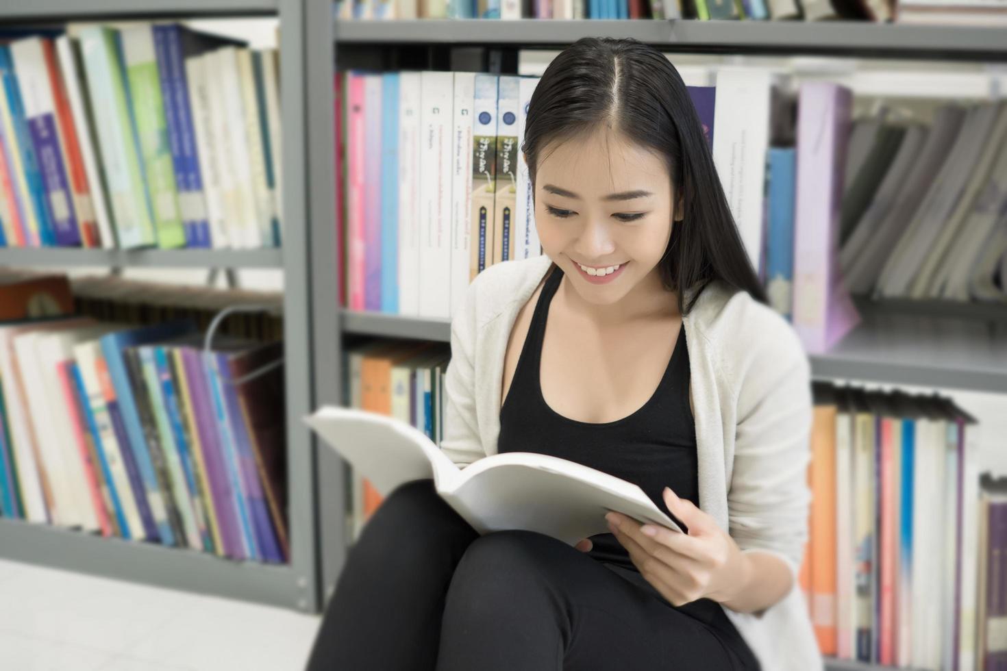 jonge Aziatische student bij de bibliotheek die een boek leest foto