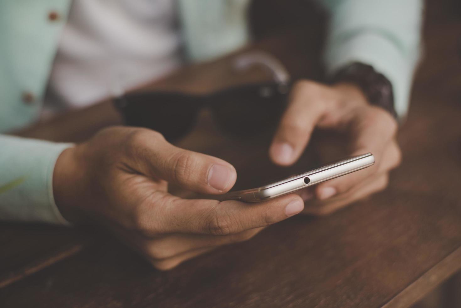 jonge hipster kerel texting met zijn mobiele telefoon aan een tafel foto