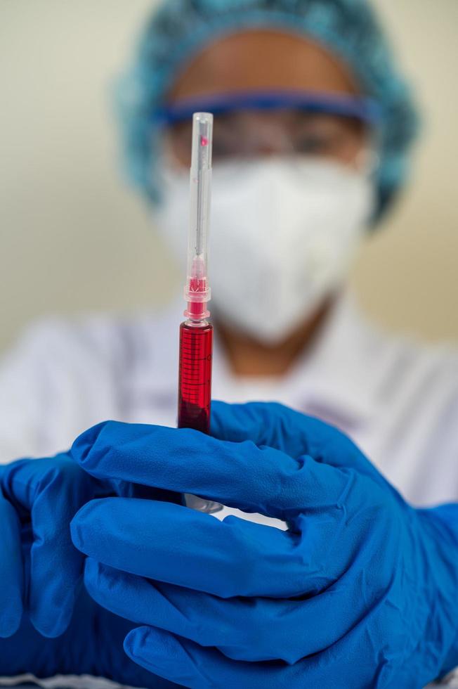 wetenschapper die beschermende maskers draagt en handschoenen die een injectiespuit met een vaccin vasthouden om covid-19 te voorkomen foto