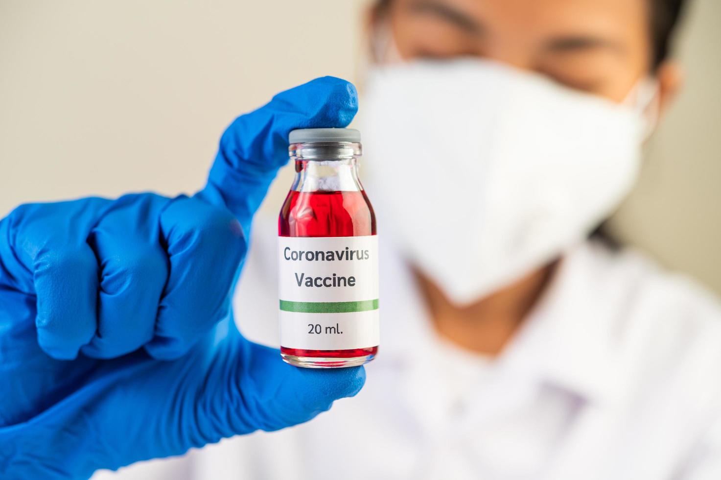 een wetenschapper met masker en handschoenen draagt flesjes met vaccins ter bescherming tegen covid-19 foto