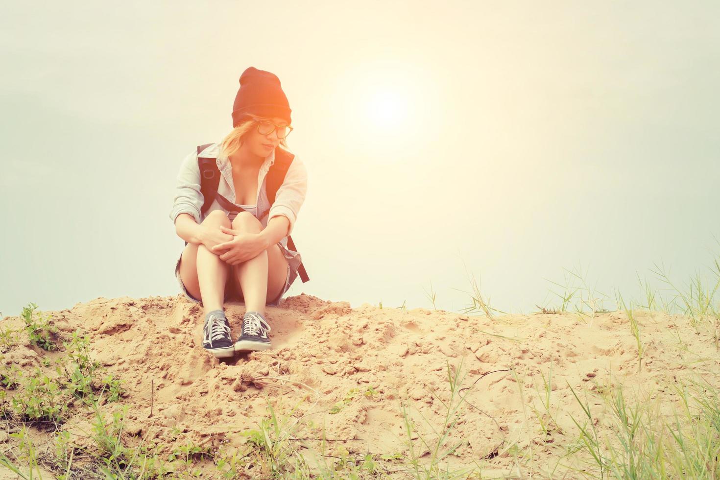 jonge hipster vrouw zittend op het zand en rugzak dragen zo verdrietig foto