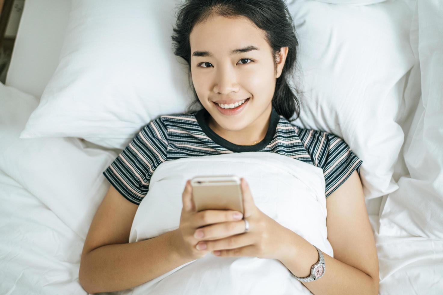 jonge vrouw met behulp van haar smartphone op bed foto