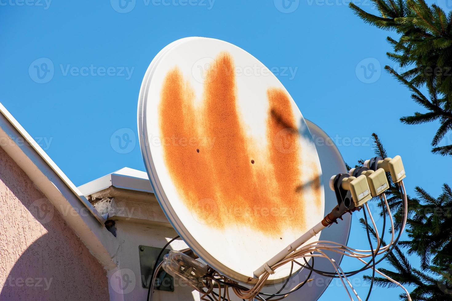 een roestig satelliet schotel Aan de muur van een rood steen gebouw. draad verbindingen zijn duidelijk zichtbaar tegen de blauw lucht. foto