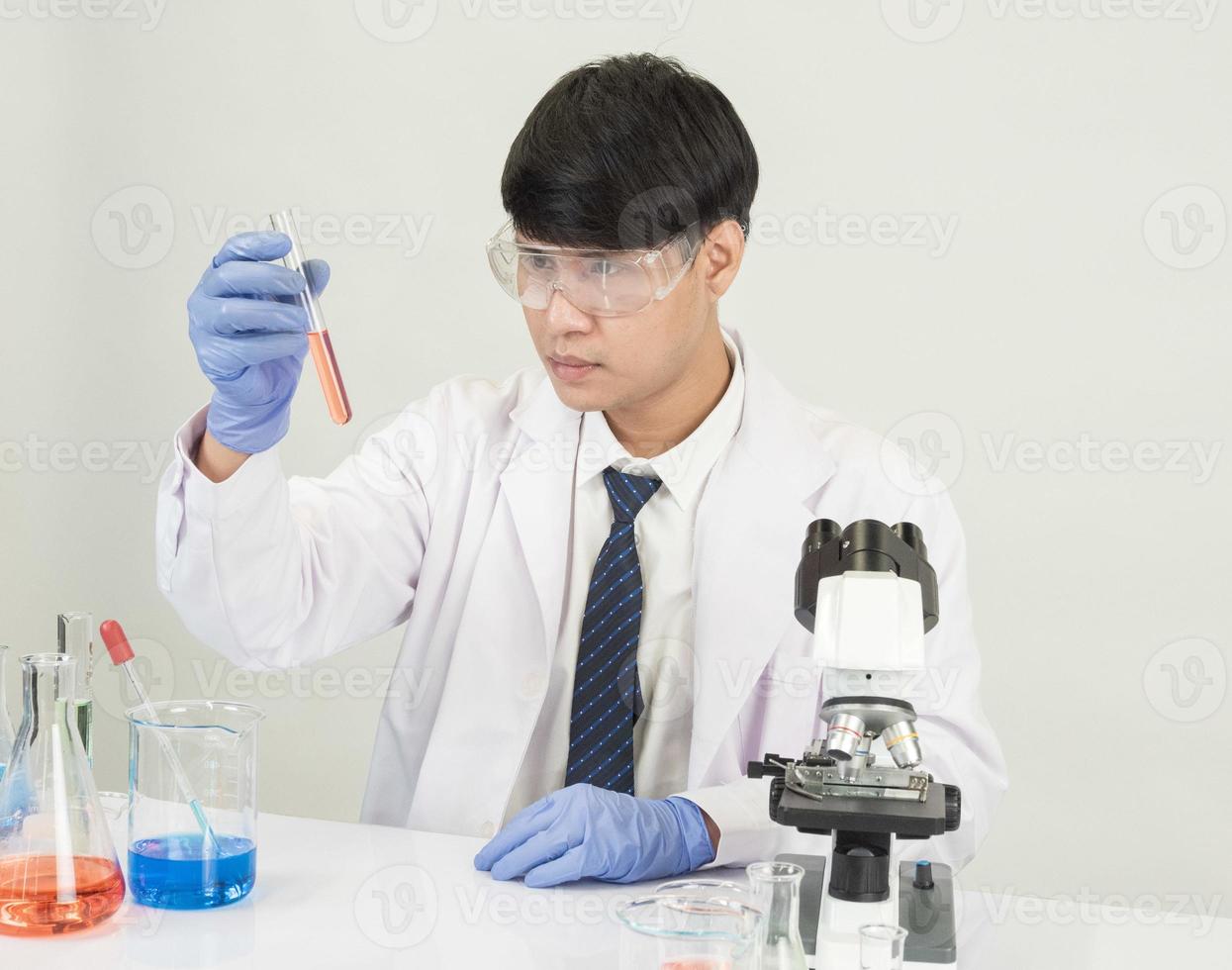Aziatisch mannetje leerling wetenschapper in reagens menging laboratorium in een wetenschap Onderzoek laboratorium met test buizen van divers maten en microscopen. Aan de tafel in laboratorium chemie laboratorium wit achtergrond. foto