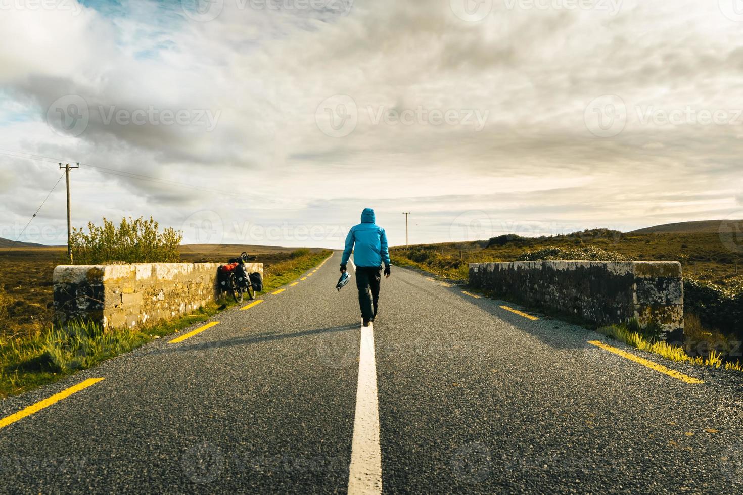 terug visie mannetje fietser in blauw jasje wandelen Aan weg door toeren fiets reizen buitenshuis in Ierland. doel en reizen avontuur concept. wild atlantic manier weg reis foto