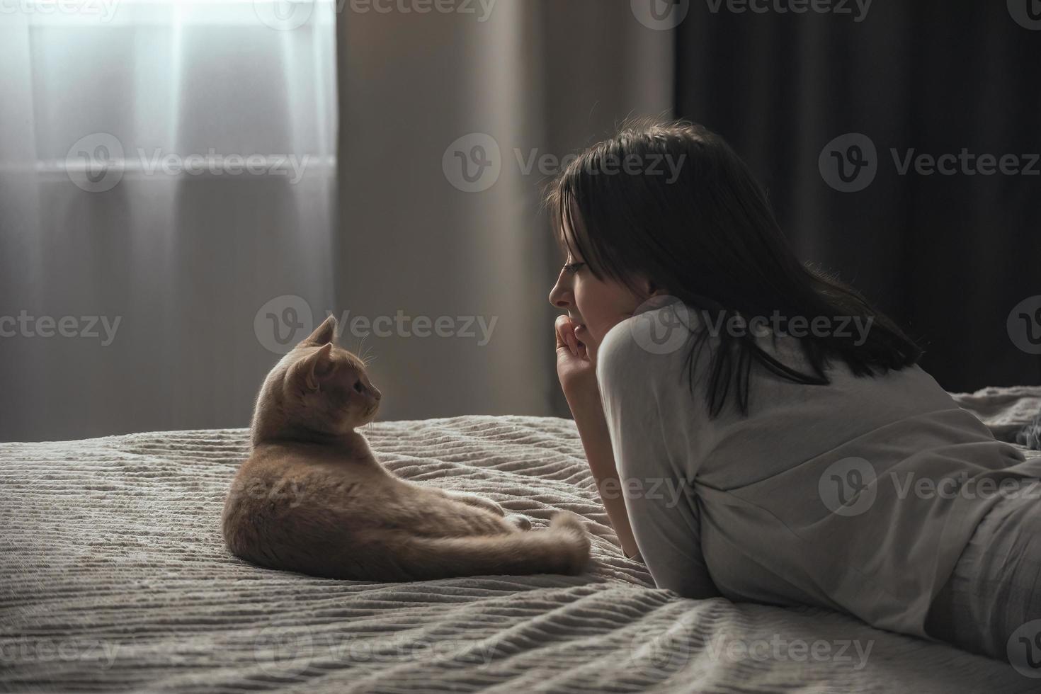 een mooi jong meisje in pyjama leugens Aan een bed Bij huis, De volgende naar haar perzik Brits kat foto