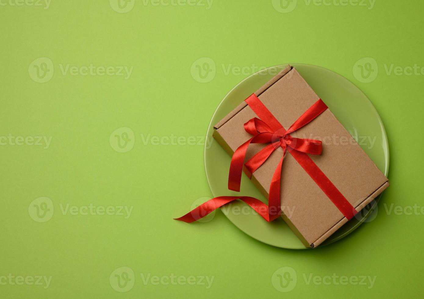 rechthoekig bruin karton doos gebonden met een rood lint en leugens Aan een groen keramisch foto