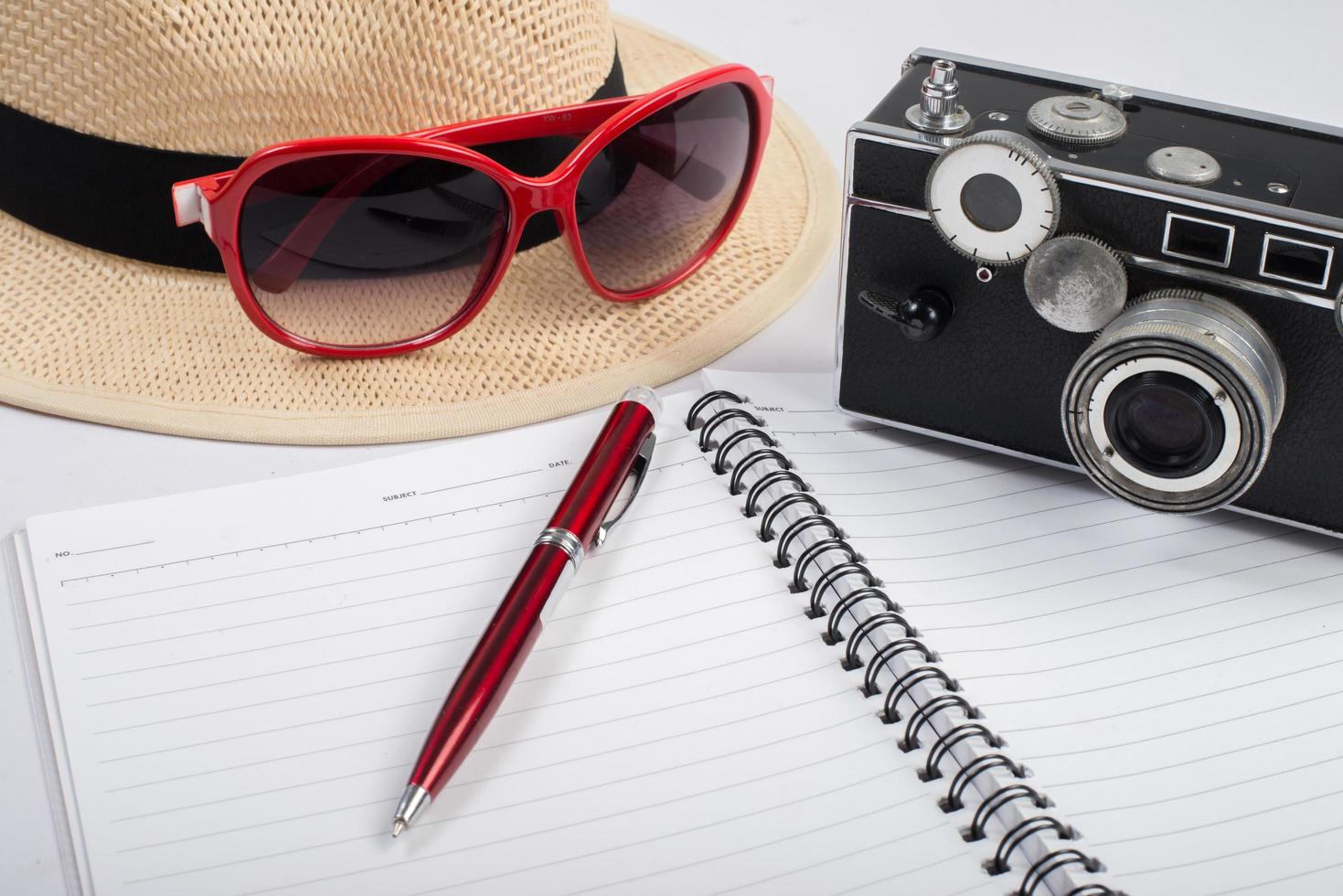 hoed, zonnebril en vintage camera met blocnote geïsoleerd op een witte achtergrond foto