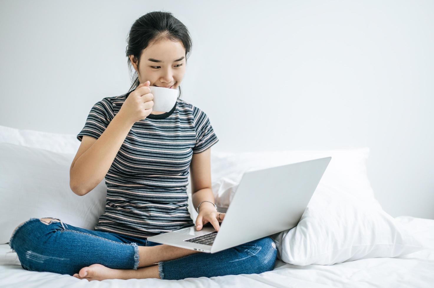 jonge vrouw koffie drinken op haar bed met laptop foto
