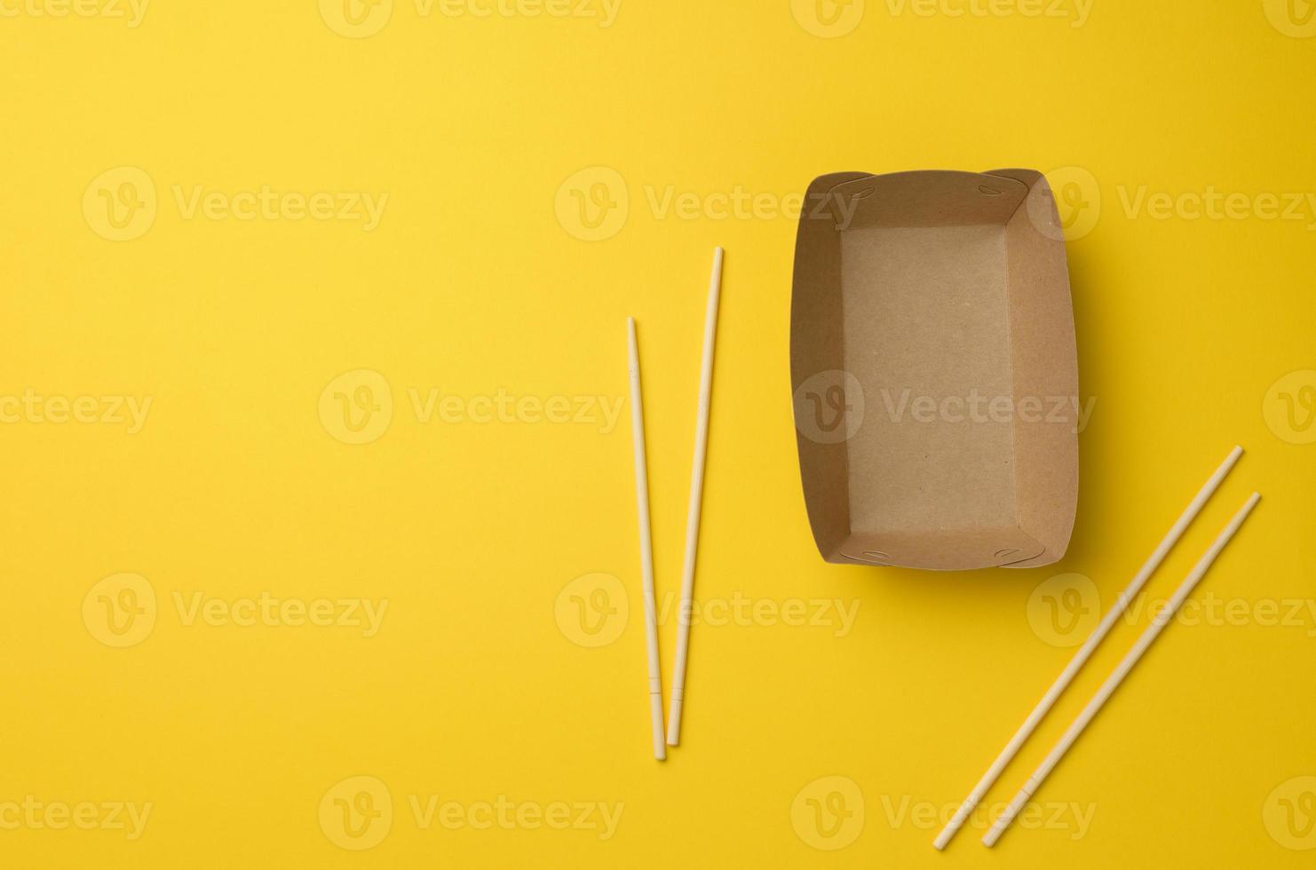 leeg bruin papier bord en houten eetstokjes Aan een geel achtergrond, top visie. beschikbaar serviesgoed foto