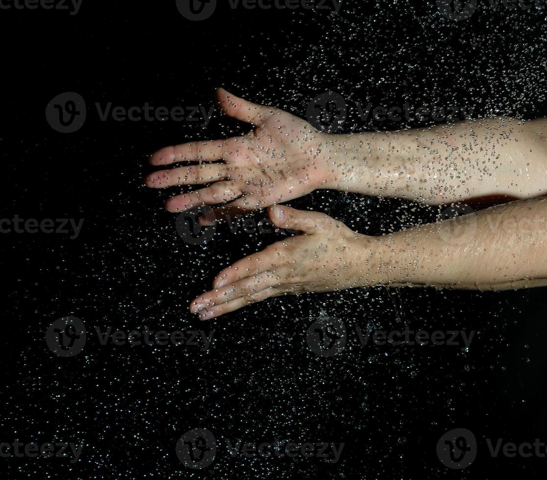 twee vrouw handen en vliegend druppels van water Aan een zwart achtergrond foto