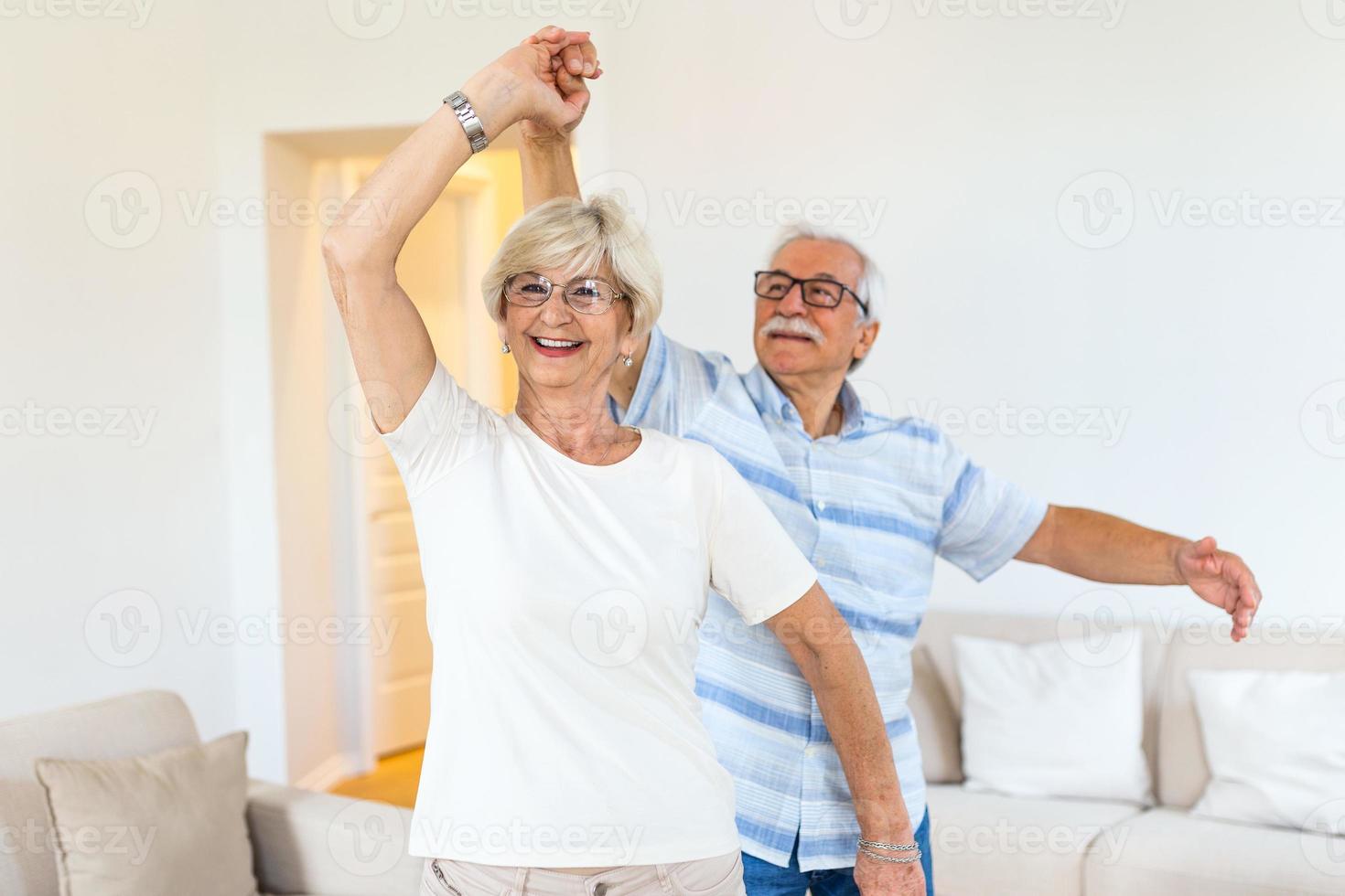 blij actief oud gepensioneerd romantisch paar dansen lachend in leven kamer, gelukkig midden- oud vrouw en ouderling man hebben pret Bij huis, glimlachen senior familie grootouders ontspannende bonding samen foto