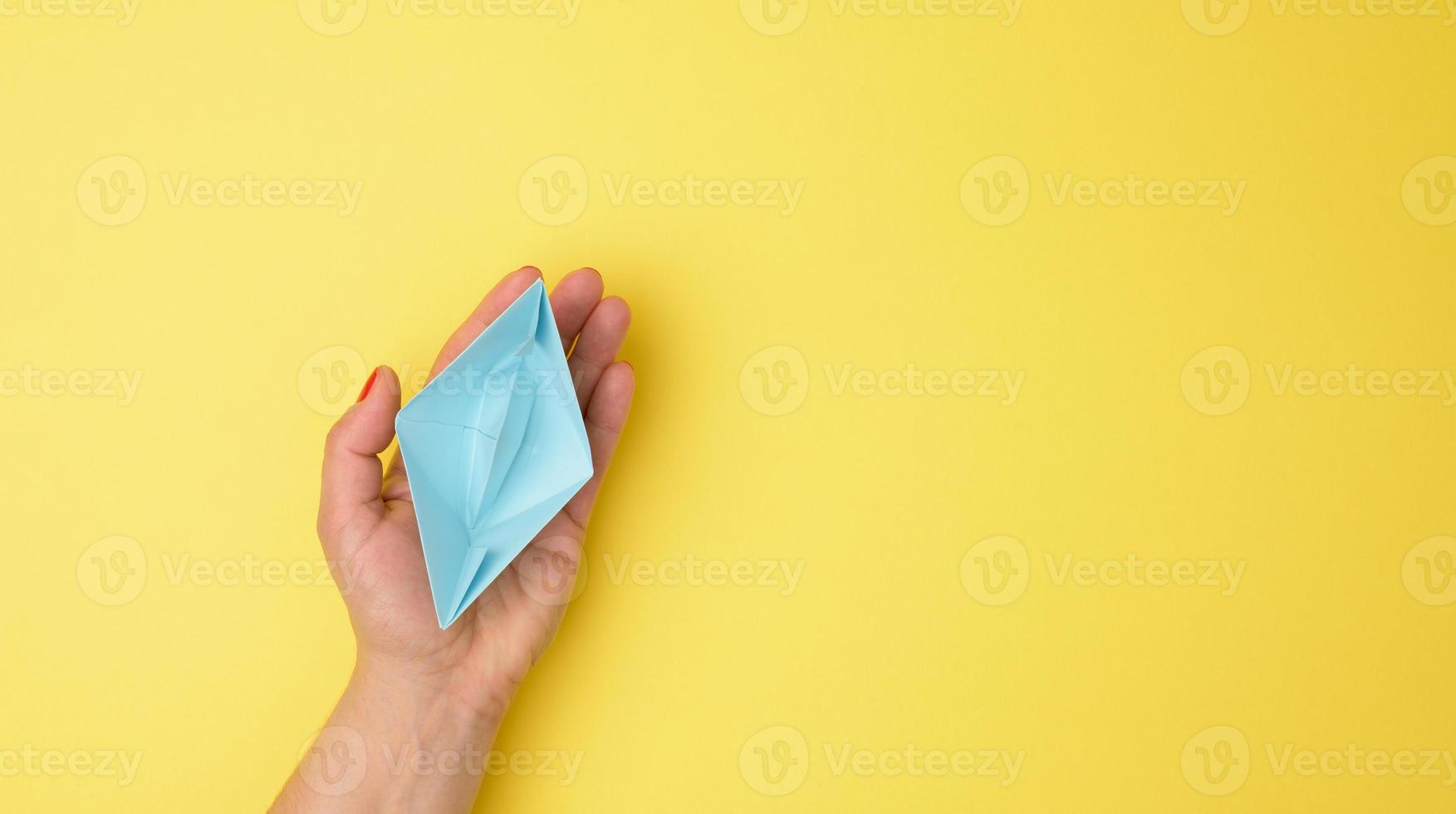 vrouw hand- houden een blauw papier boot Aan een geel achtergrond. begeleiding en ondersteuning concept foto