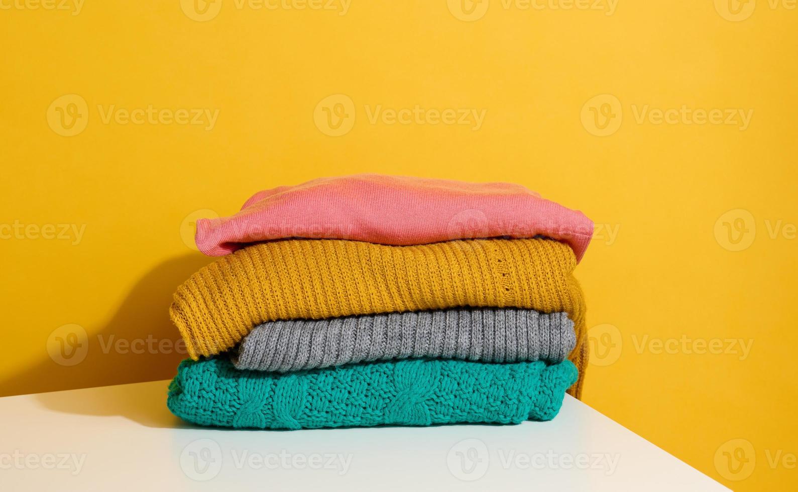 stack van gevouwen gebreid truien Aan geel achtergrond. comfortabel kleren, wassen foto