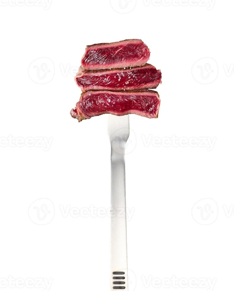 gebakken biefstuk stukken geregen Aan een groot metaal vork en geïsoleerd Aan een wit achtergrond foto