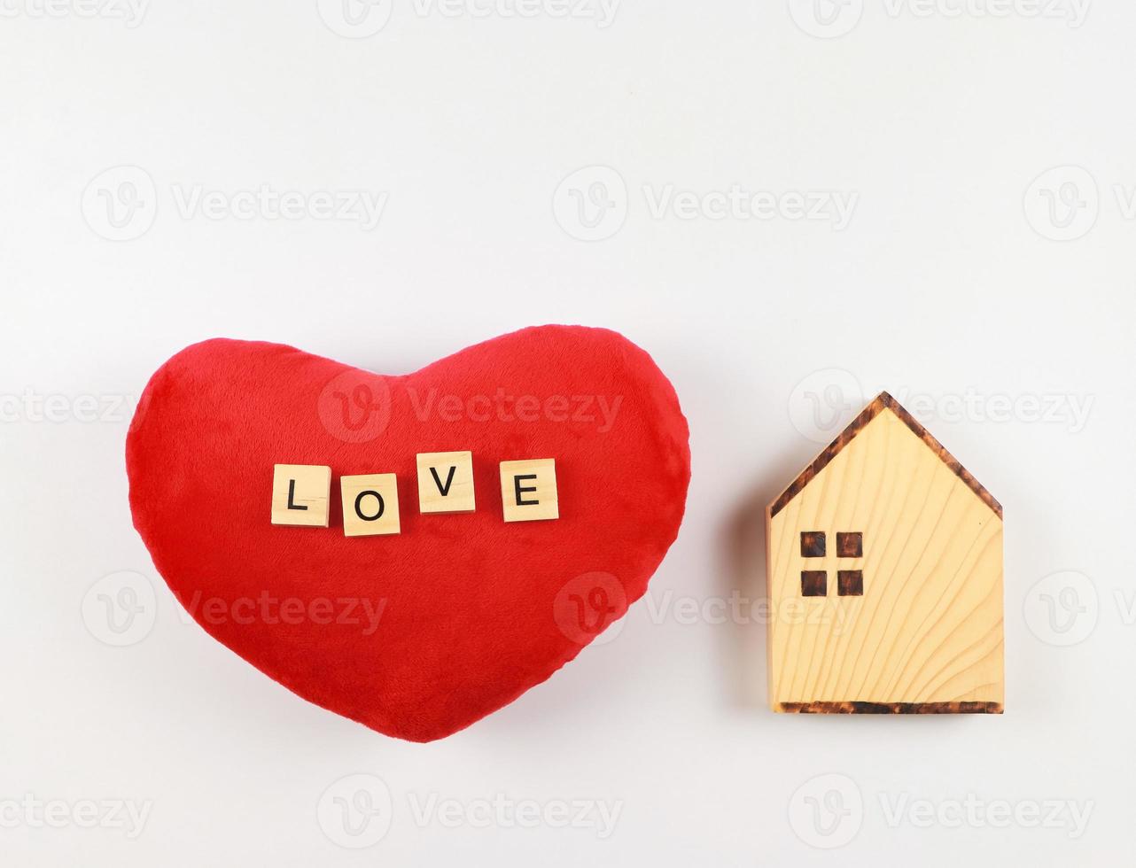 vlak lay-out van houten model- huis en rood hart vorm hoofdkussen met houten brieven l O v e geïsoleerd Aan wit achtergrond met kopiëren ruimte, valentijnsdag of huis van liefde concept. foto