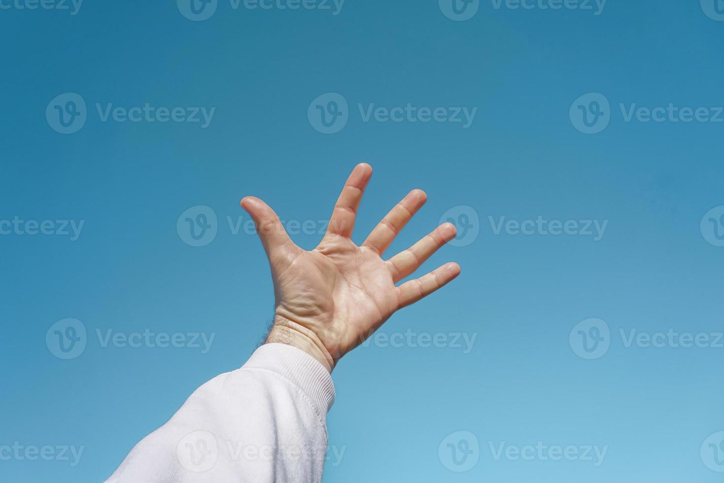 hand- omhoog in de lucht gebaren in de blauw lucht, blauw achtergrond foto