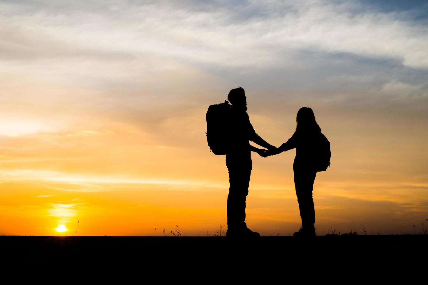 silhouetten van twee wandelaars met rugzakken die van de zonsondergang genieten foto