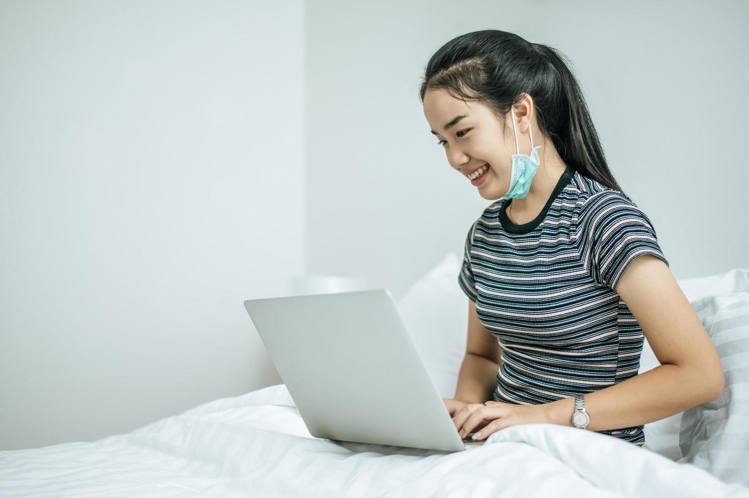 een jonge vrouw die op haar laptop in bed speelt foto