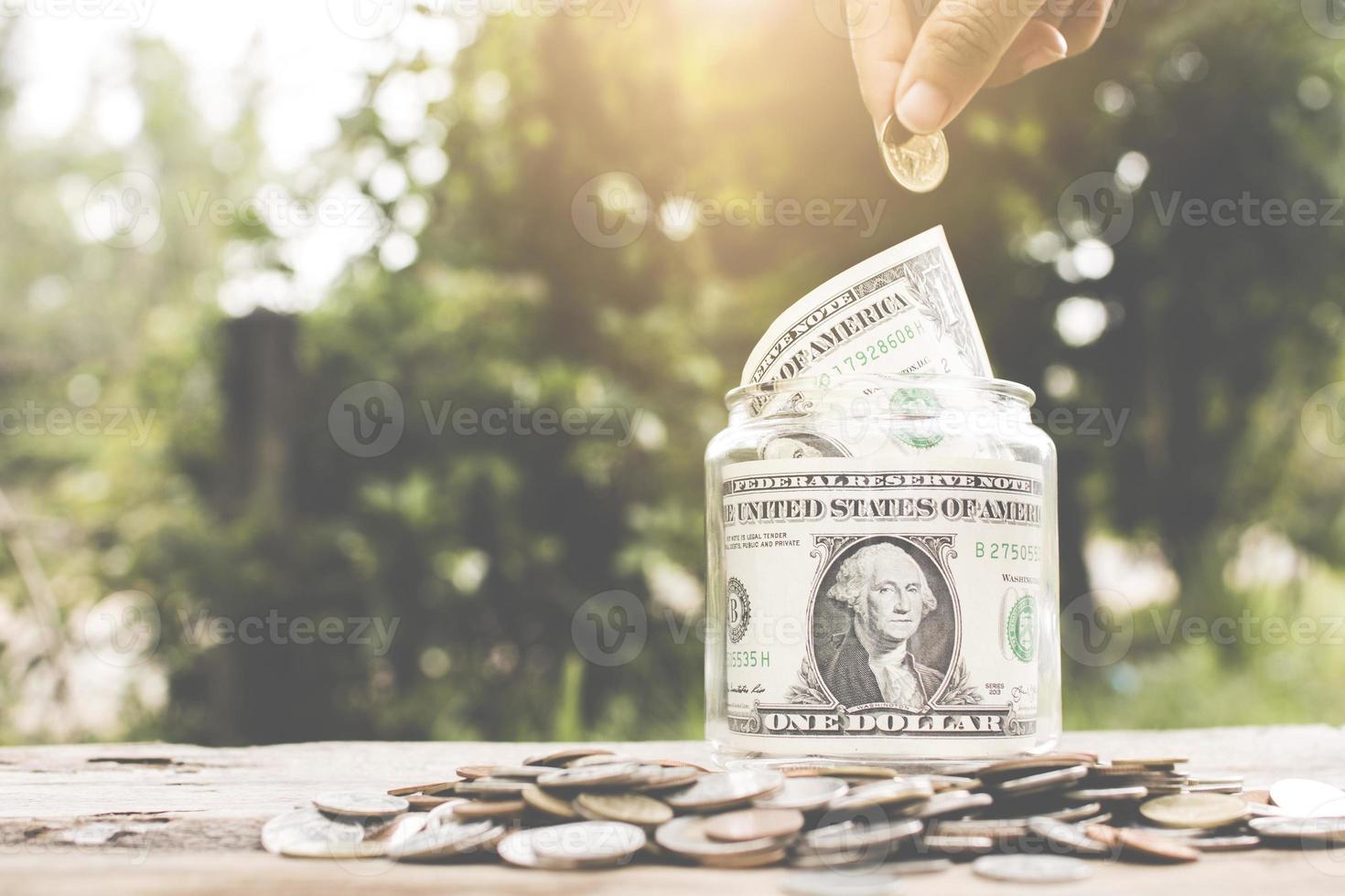 geld concept opslaan, hand geld steken in glazen pot foto
