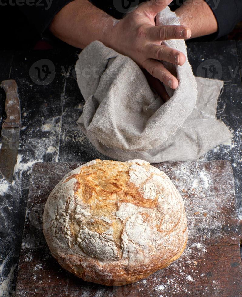 gebakken ronde brood Aan een bord, achter de koken in zwart kleren foto