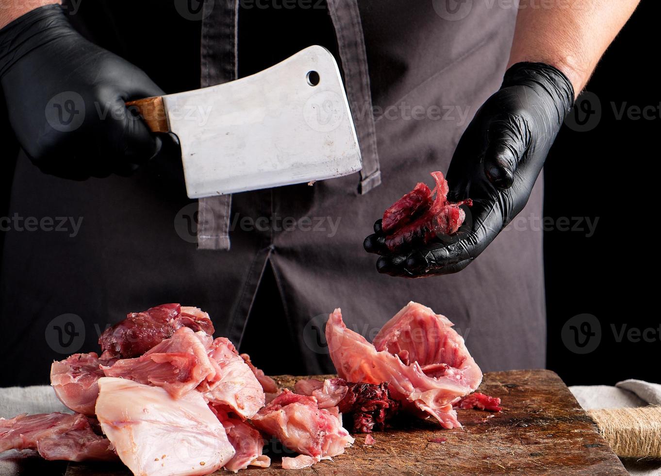 chef in zwart latex brokken bezuinigingen in stukken rauw konijn vlees Aan een bruin houten bord foto