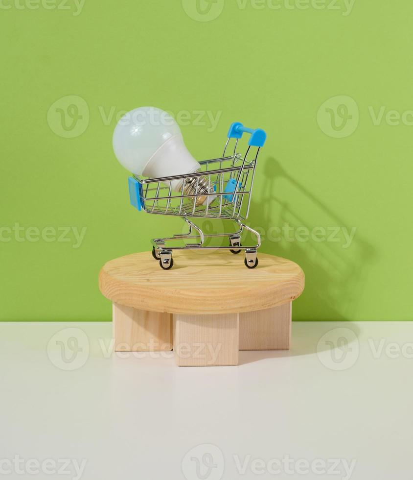 een miniatuur ijzer kar en een glas wit lamp Aan een groen achtergrond. buying en verkoop elektriciteit, korting foto