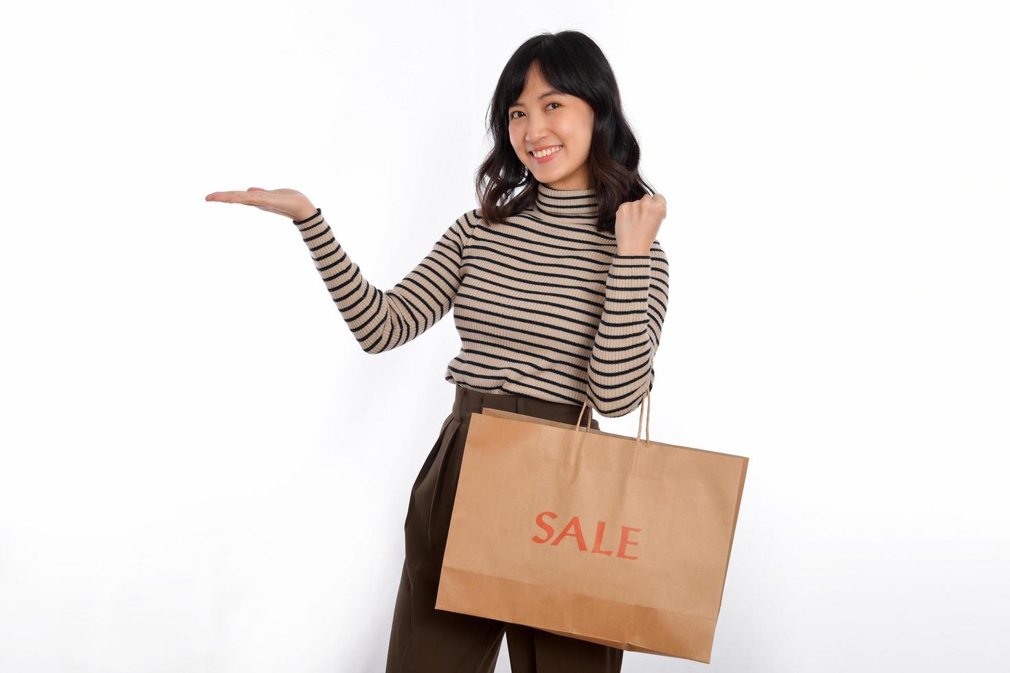 gelukkig jong Aziatisch vrouw gewoontjes uniform Holding boodschappen doen papier zak geïsoleerd Aan wit achtergrond. boodschappen doen korting concept foto