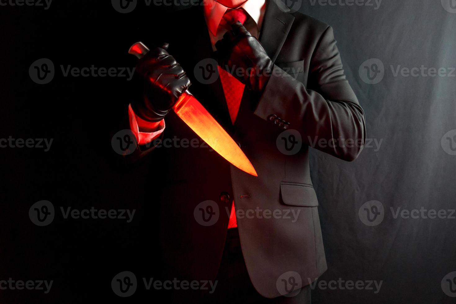 zakenman in donker pak en rood stropdas Holding scherp mes Aan zwart achtergrond. halloween verschrikking film moordenaar. foto