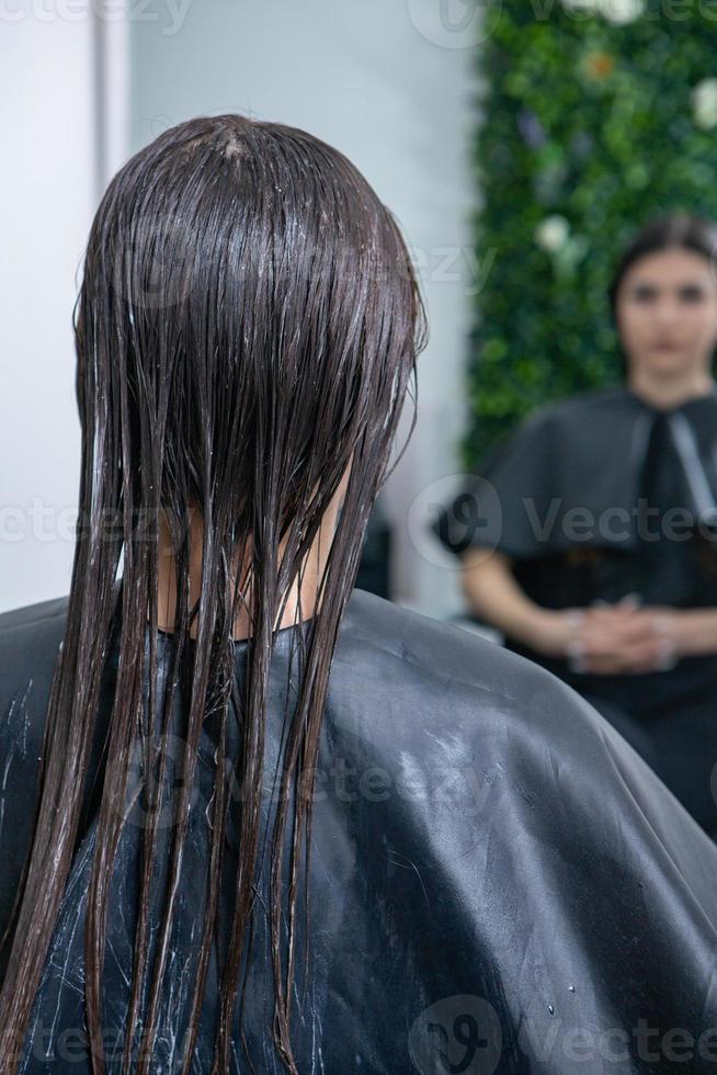 kapper is van toepassing een haar- masker naar Rechtdoor zwart haar. haar- zorg Bij de schoonheid salon. foto