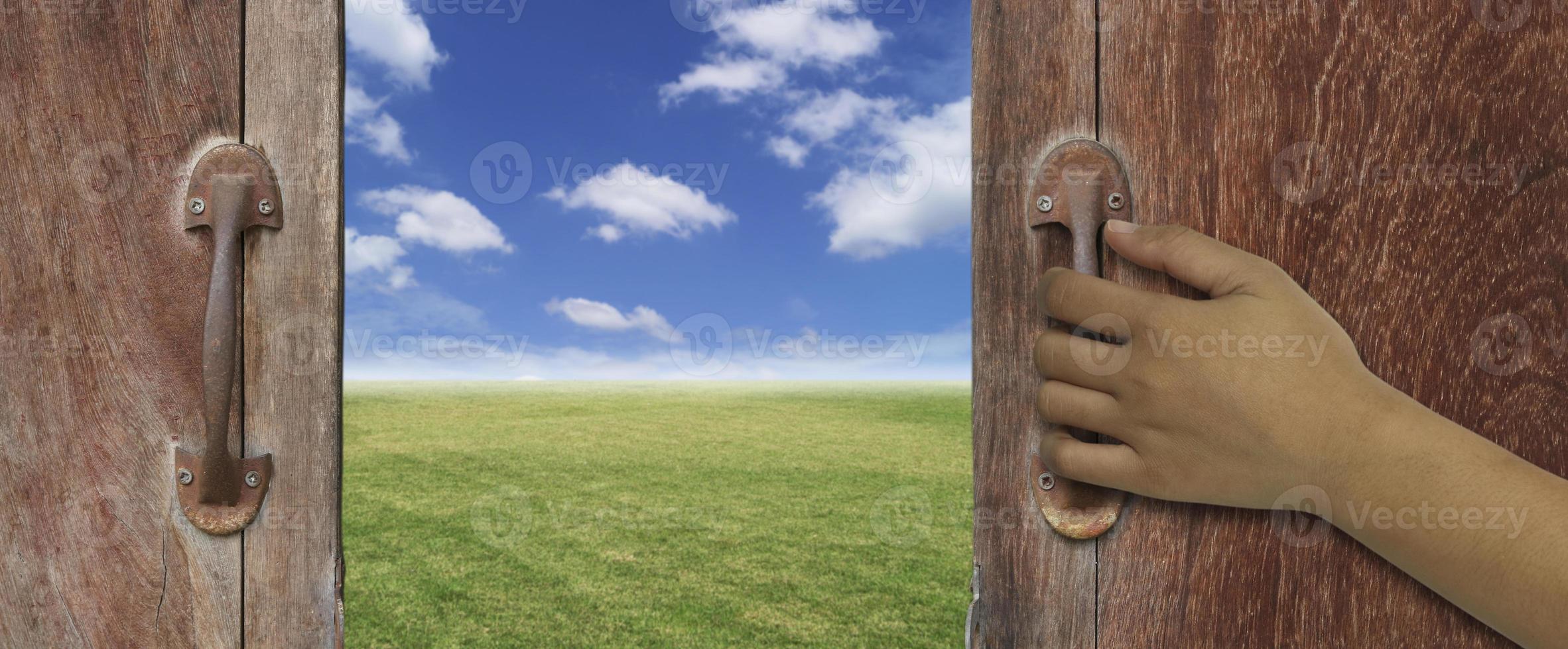 hand openen van een houten deur naar prachtige buitenlucht foto