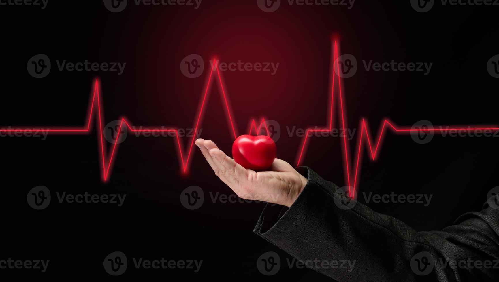 mannetje hand- Holding een rood hart Aan een donker achtergrond, vroeg diagnose van de cardiovasculair systeem foto