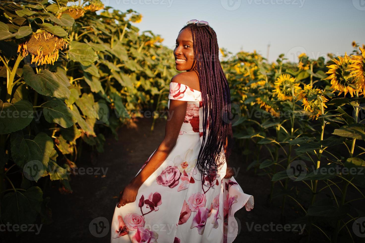 mooie jonge zwarte vrouw draagt zomerjurk pose in een zonnebloemveld. foto