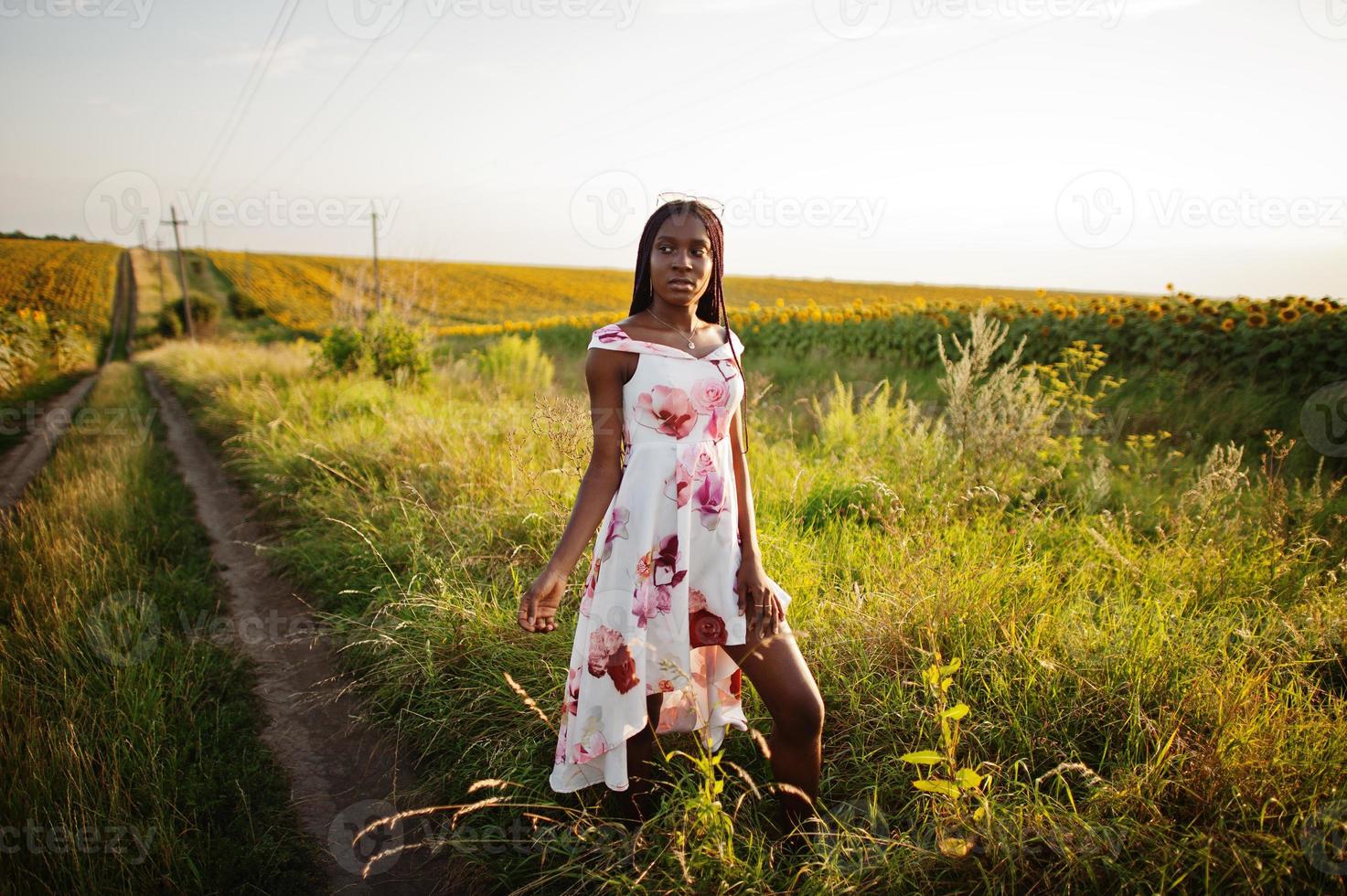 mooie jonge zwarte vrouw draagt zomerjurk pose in een zonnebloemveld. foto