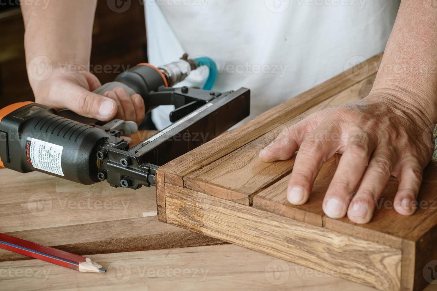 timmerman met spijkerpistool of brad spijkergereedschap op houten kist in een werkplaats, meubelrestauratie houtbewerkingsconcept. selectieve focus foto