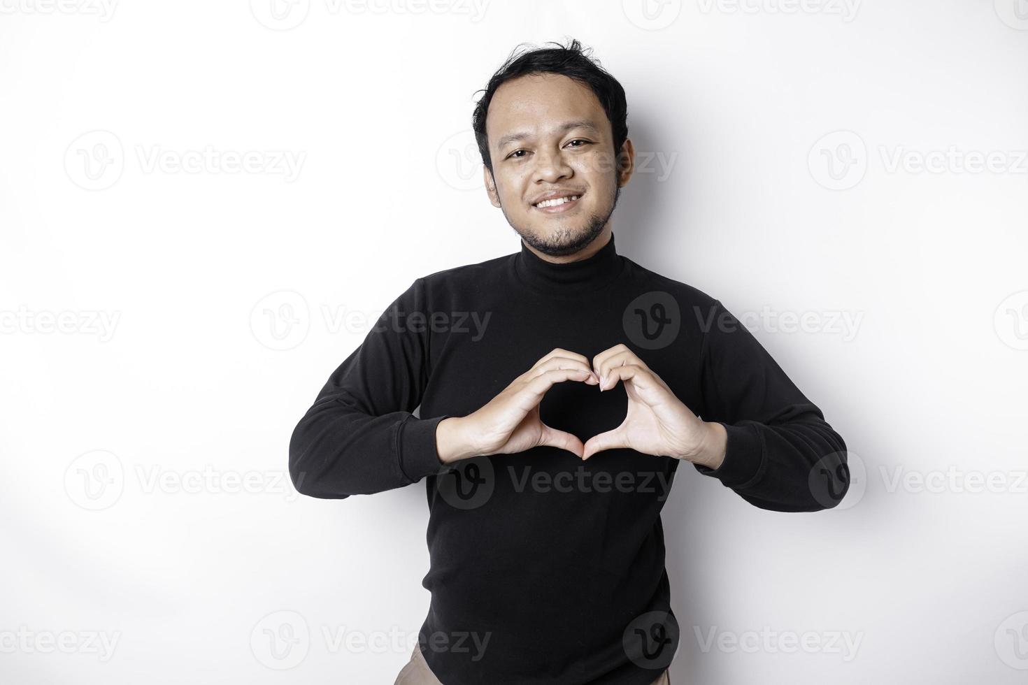 een gelukkig jong Aziatisch Mens vervelend een zwart overhemd voelt romantisch vormen hart gebaar uitdrukken inschrijving gevoelens foto