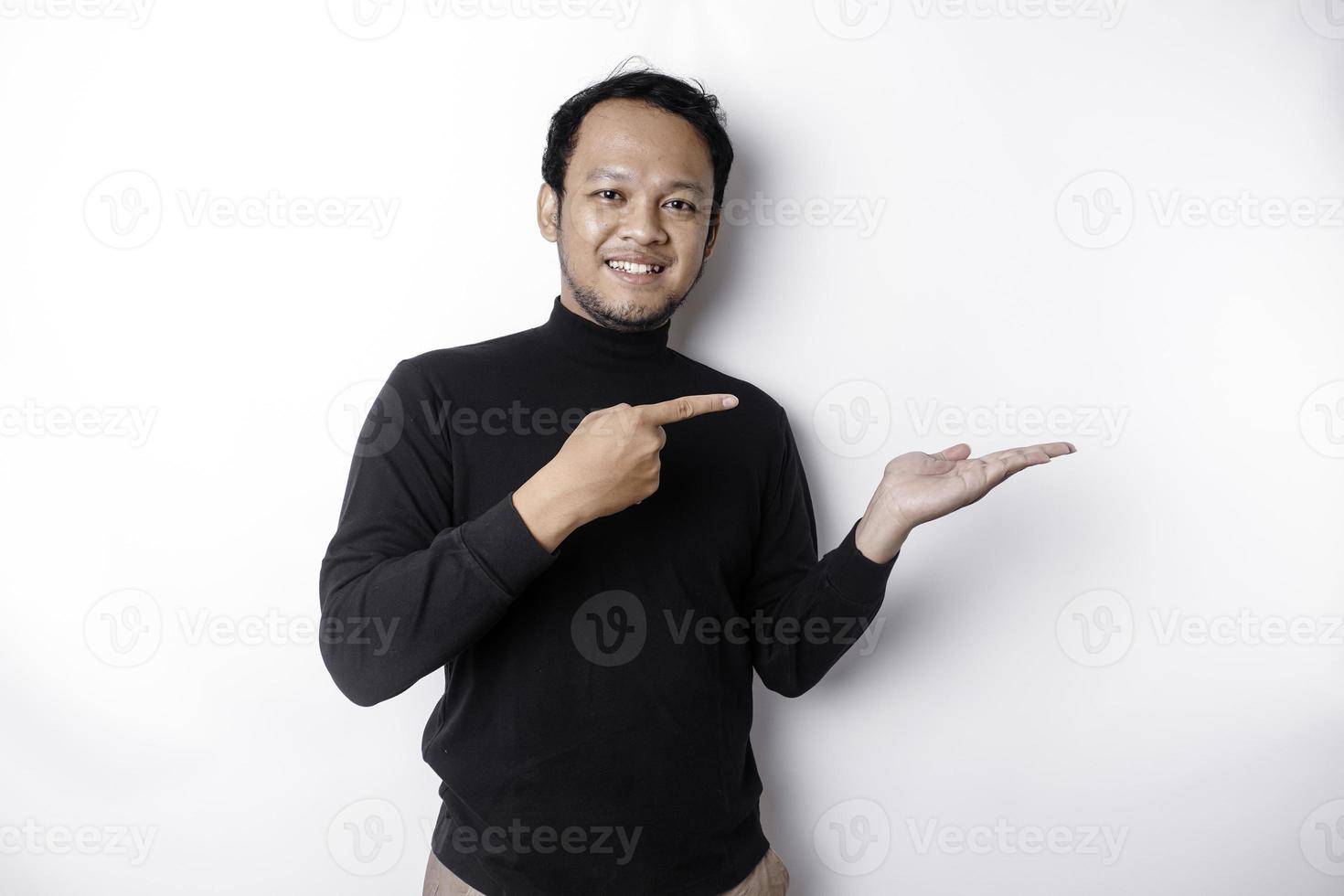 opgewonden Aziatisch Mens vervelend zwart overhemd richten Bij de kopiëren ruimte naast hem, geïsoleerd door wit achtergrond foto
