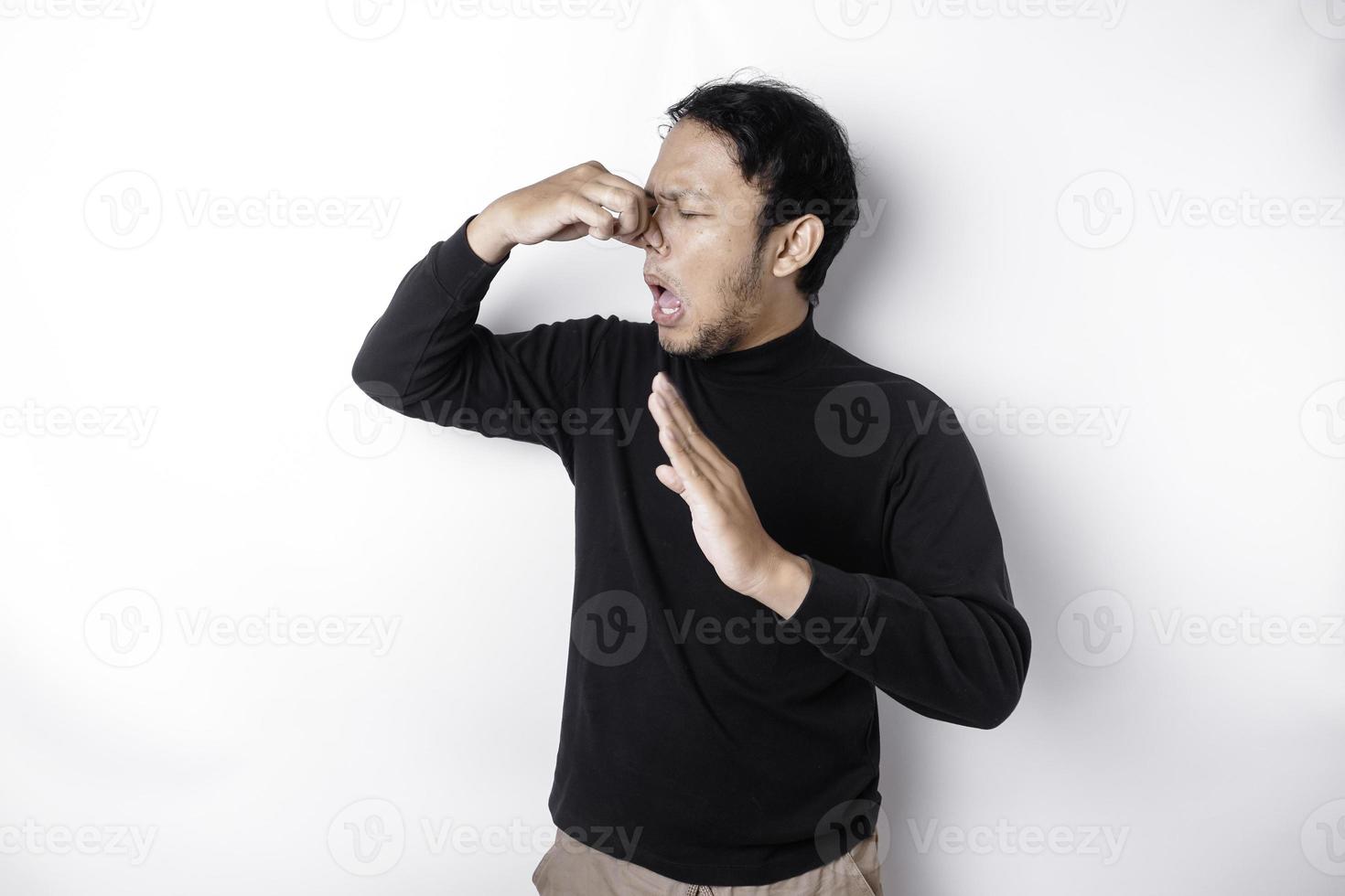 jong Aziatisch Mens vervelend t-shirt staand over- geïsoleerd wit achtergrond ruiken iets stinkend en afschuwelijk, ondraaglijk geur, Holding adem met vingers Aan neus. slecht ruikt concept. foto