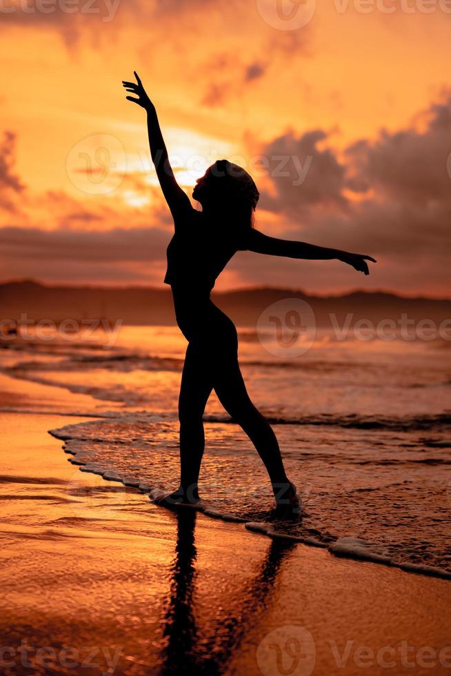 silhouet van een heel slank ballerina aan het doen ballet praktijk alleen Aan de kust met golven crashen Bij haar foto