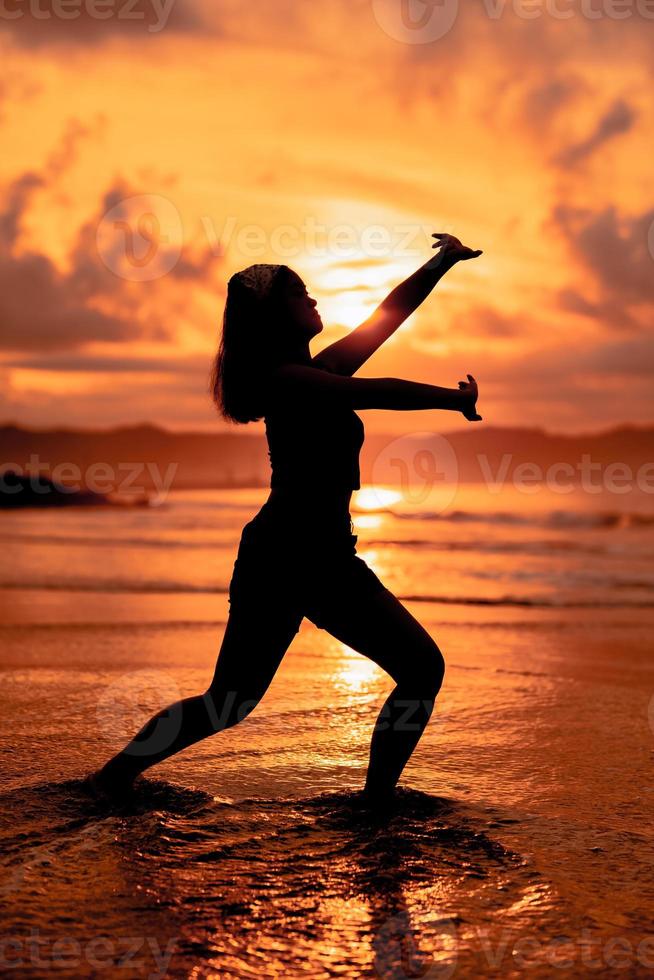 de silhouet van een Aziatisch tiener in zwart kleren poseren met haar lichaam bovenstaand de kust golven heel prachtig foto