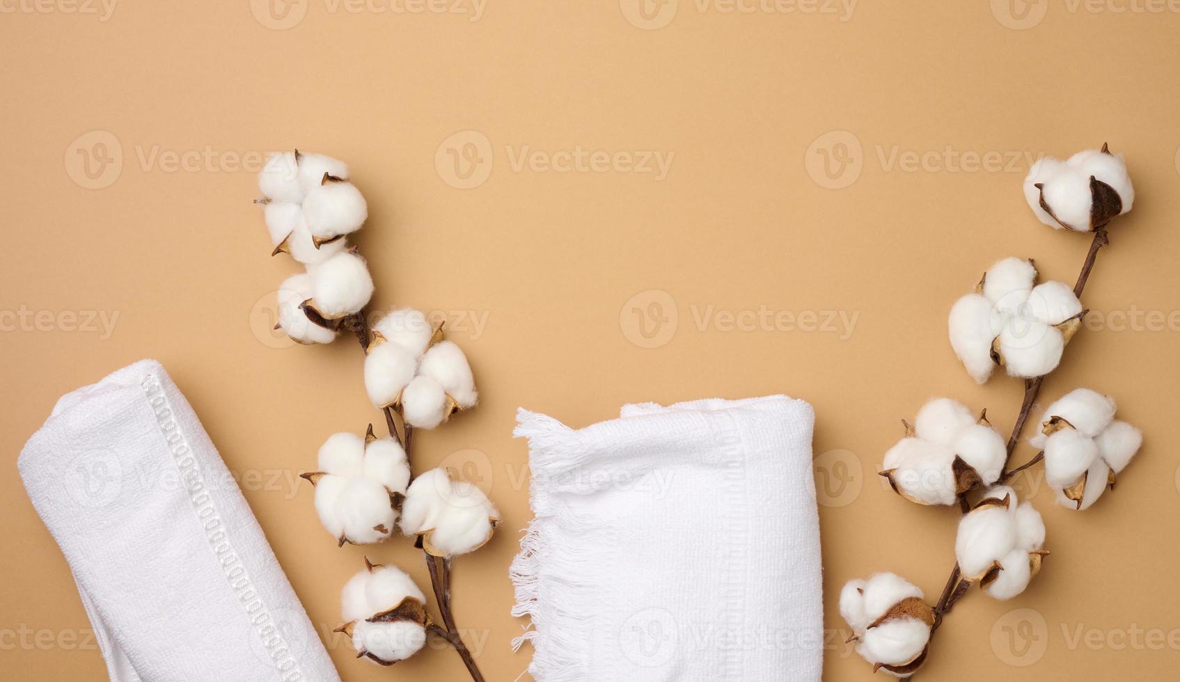 gevouwen wit katoen badstof handdoek en takjes van katoen bloem Aan een licht bruin achtergrond, top visie foto
