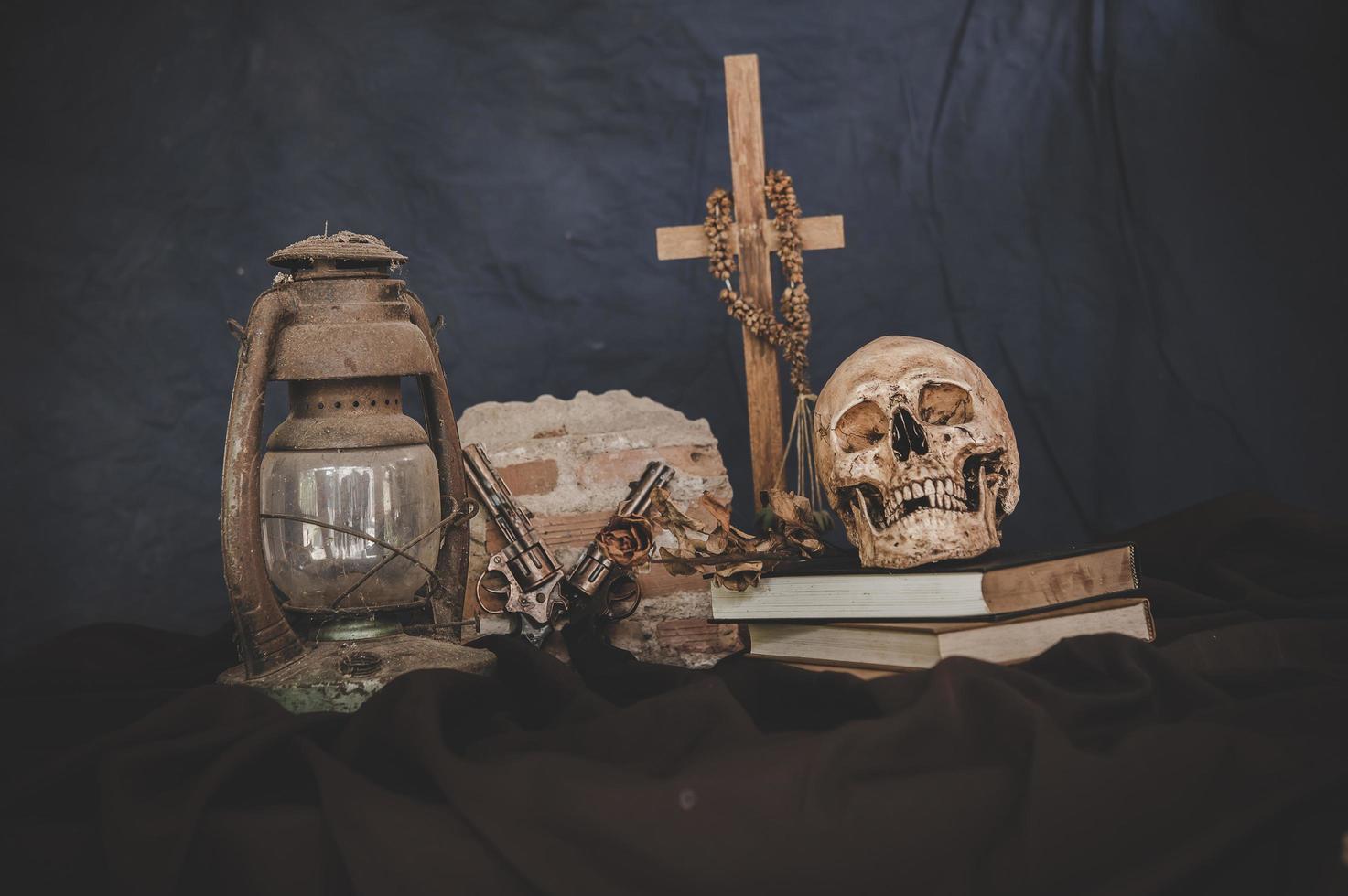 stilleven met schedels op boeken, oude lampen, droge bloemen en gekruiste geweren foto