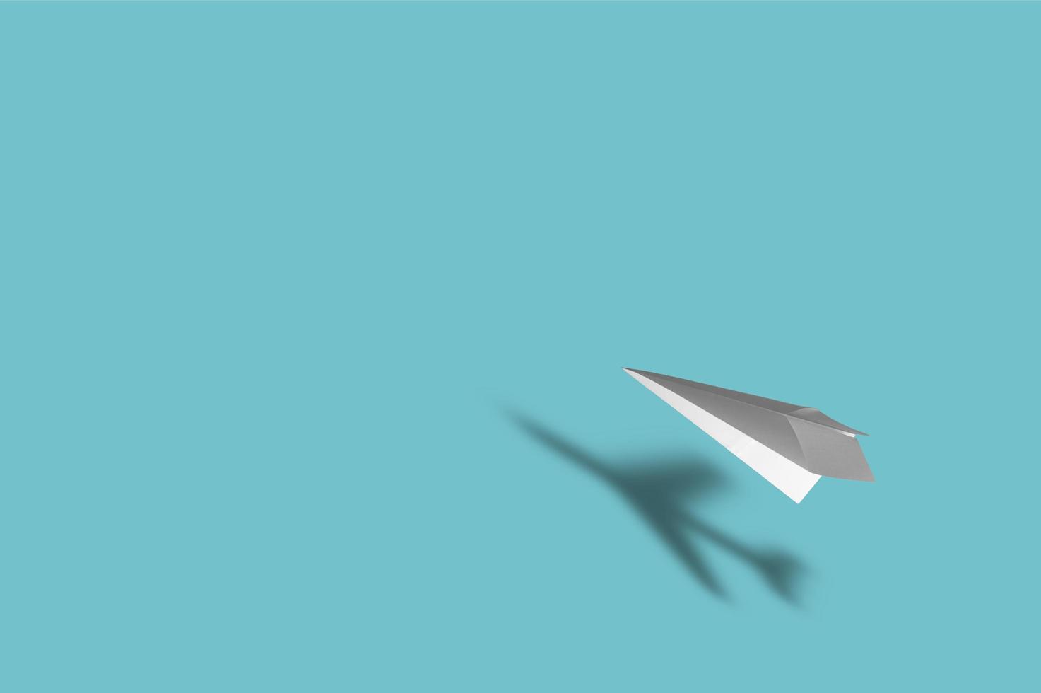 papieren vliegtuigje met de schaduw van een echt vliegtuig op blauwe achtergrond foto