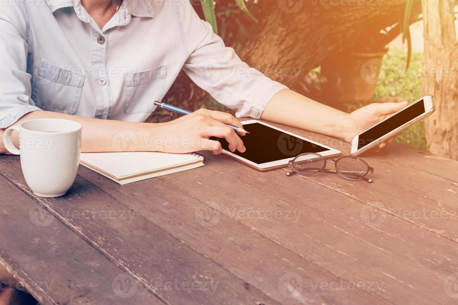 vrouw gebruik makend van telefoon Aan tafel hout in tuin Bij koffie winkel met wijnoogst afgezwakt. foto