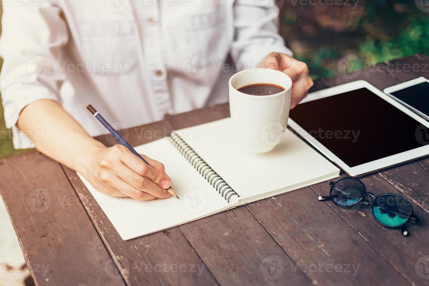 jong bedrijf vrouw hand- met potlood schrijven Aan notebook. vrouw hand- met potlood schrijven Aan notitieboekje en werken Bij koffie winkel. foto