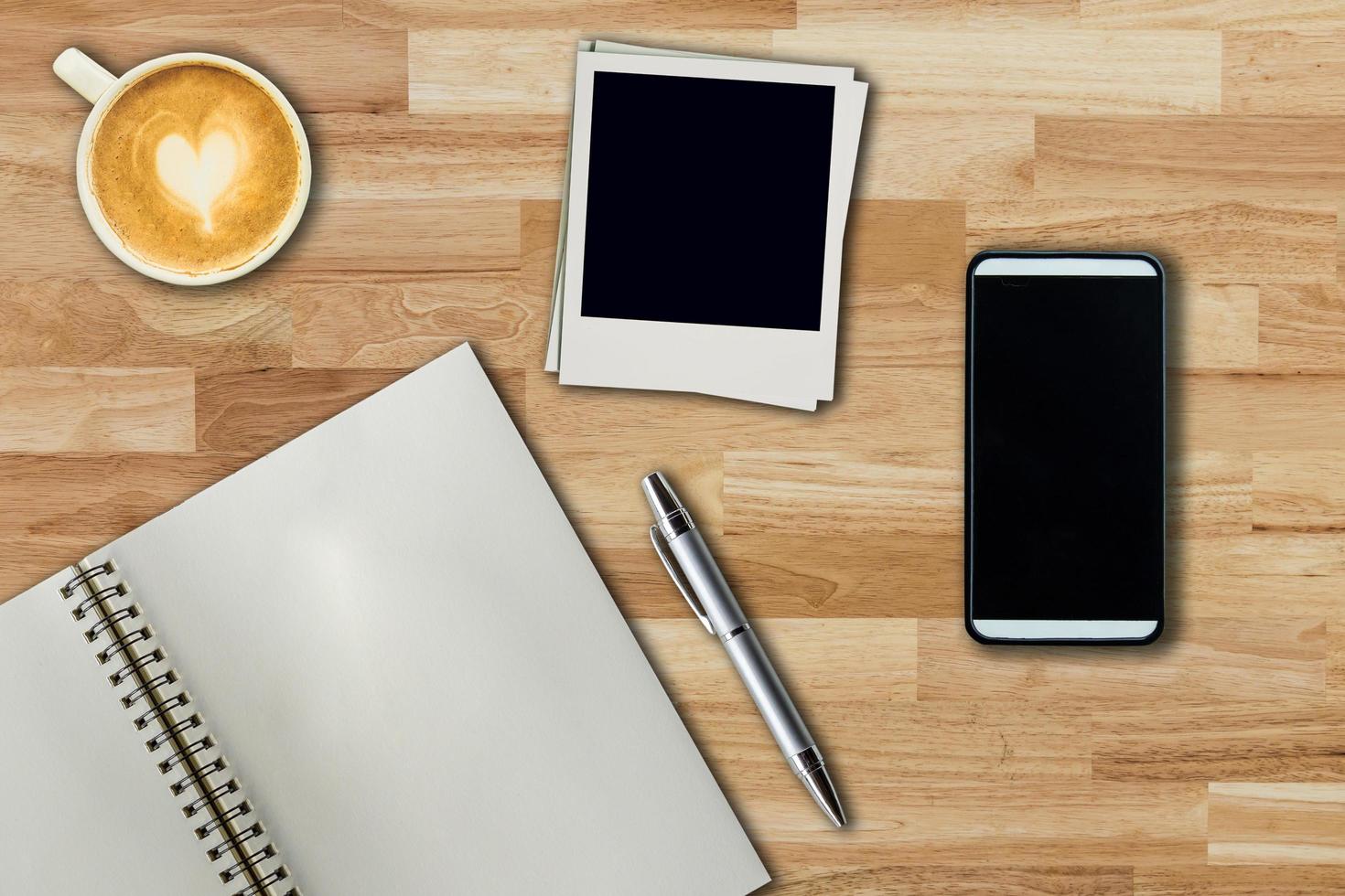 mobiel telefoon, notitieboekje pen, foto kader en koffie kop Aan kantoor houten tafel met kopiëren ruimte.