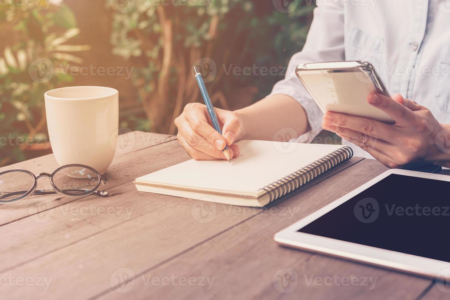 dichtbij omhoog hand- vrouw schrijven notitieboekje in koffie winkel met wijnoogst afgezwakt. foto