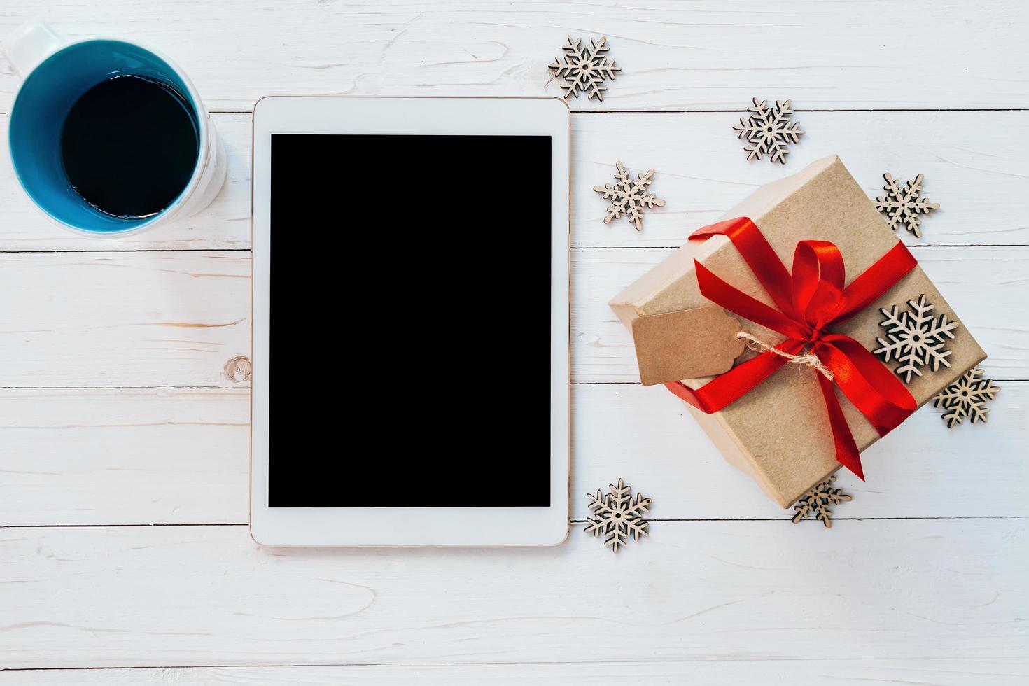 top visie tablet, kop koffie, en geschenk doos met sneeuwvlokken Aan wit hout achtergrond voor Kerstmis en nieuw jaar. foto