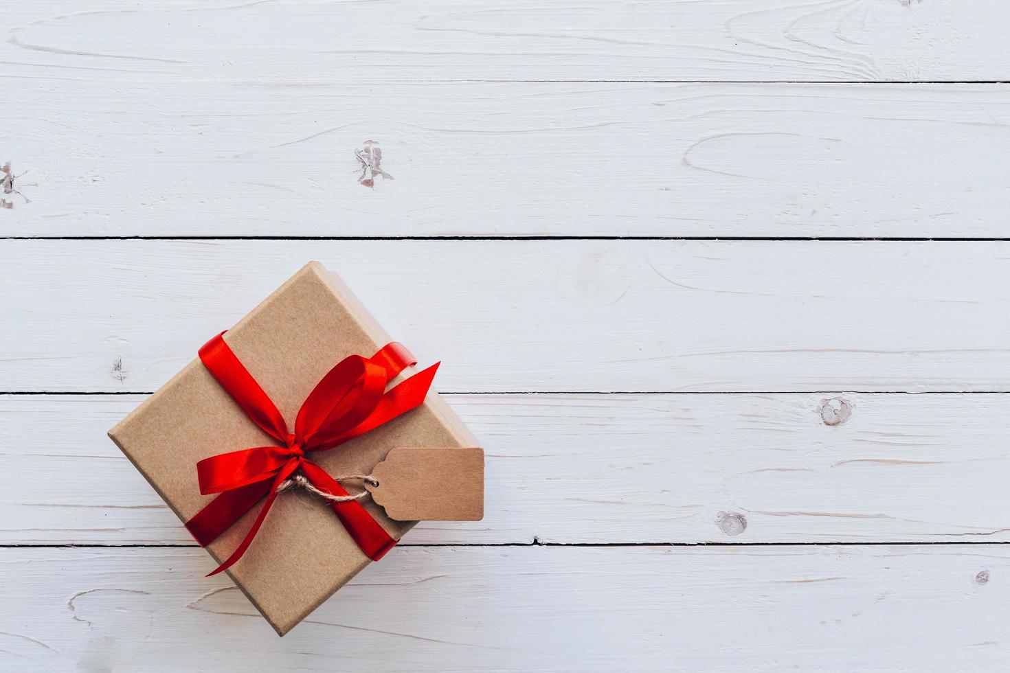 bovenstaand bruin geschenk doos met label Aan houten bord achtergrond. geschenk doos met rood lint Aan houten wit achtergrond met ruimte. foto