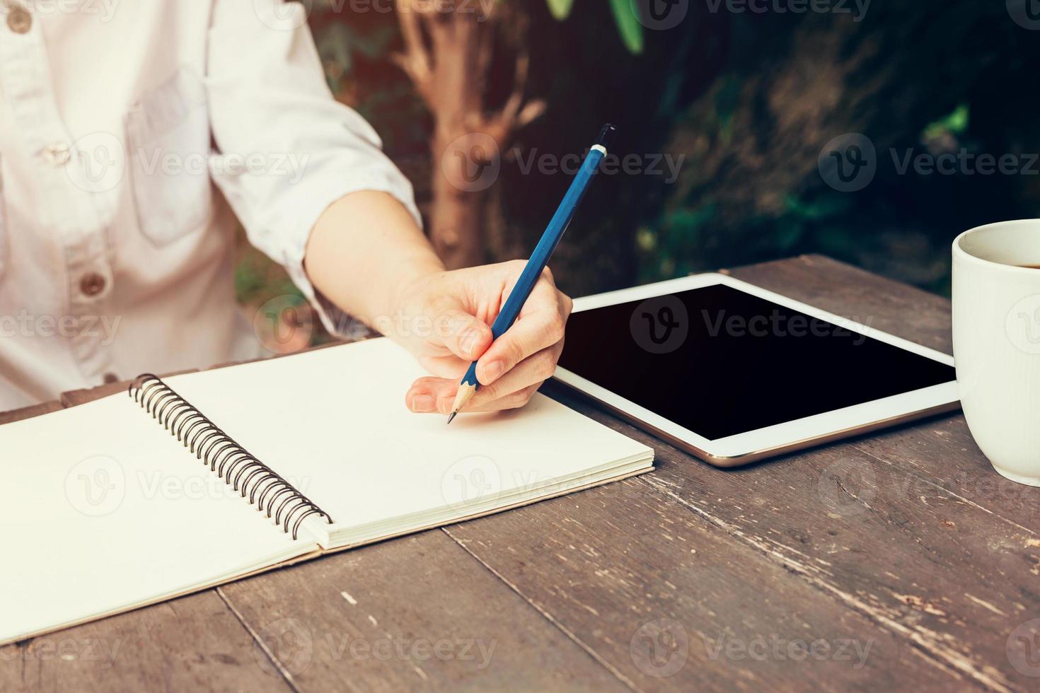 jong bedrijf vrouw hand- met potlood schrijven Aan notebook. vrouw hand- met potlood schrijven Aan notitieboekje en werken Bij koffie winkel. foto